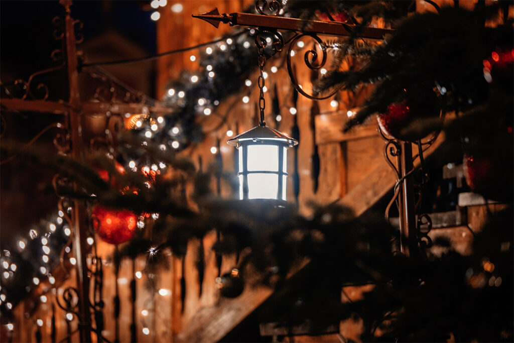 A close-up of a warmly lit lantern hanging among festive holiday decorations, including string lights and ornaments. The scene, meticulously cleaned by SUDS Power Washing, has a cozy, rustic feel with blurred background elements adding to the ambiance.